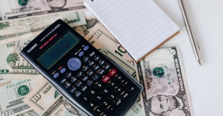 Credit Strategies - From above electronic calculator and notepad placed over United States dollar bills together with metallic pen for budget planning and calculation