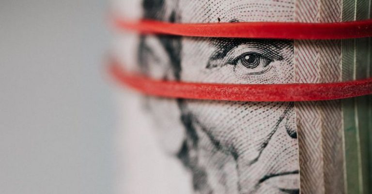 Currency Fluctuations - Closeup of rolled United States five dollar bills tightened with red rubber band