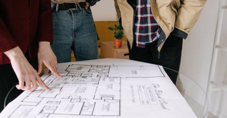 Property Selling - Three People Standing Near Blueprint on Glass Table