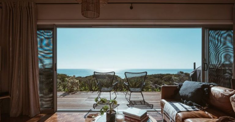 Ultra-Luxury Properties - Interior design of luxurious apartment with large balcony doors and wooden terrace having picturesque view on green forested seashore and calm blue sea