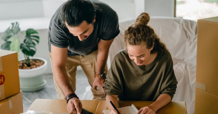 Real Estate Investments - Cheerful diverse couple writing in notebook near boxes before relocation